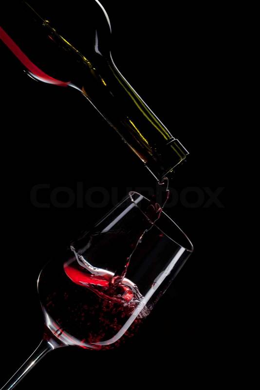 Red wine pouring into wine glass isolated on black, stock photo