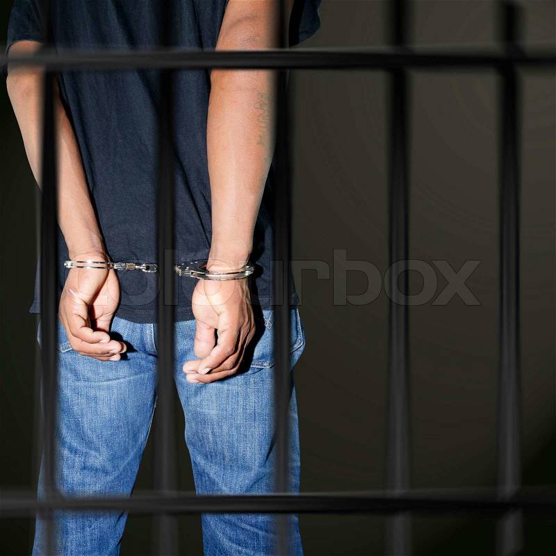 Prisoner locked in handcuffs in prison on black background, stock photo