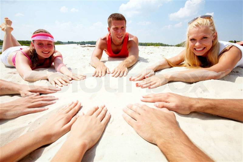 Image of several teens lying on beach and keeping their hands on sand in the form of circle, stock photo