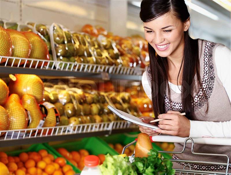 Image of pretty woman choosing products in supermarket with list of things to buy, stock photo