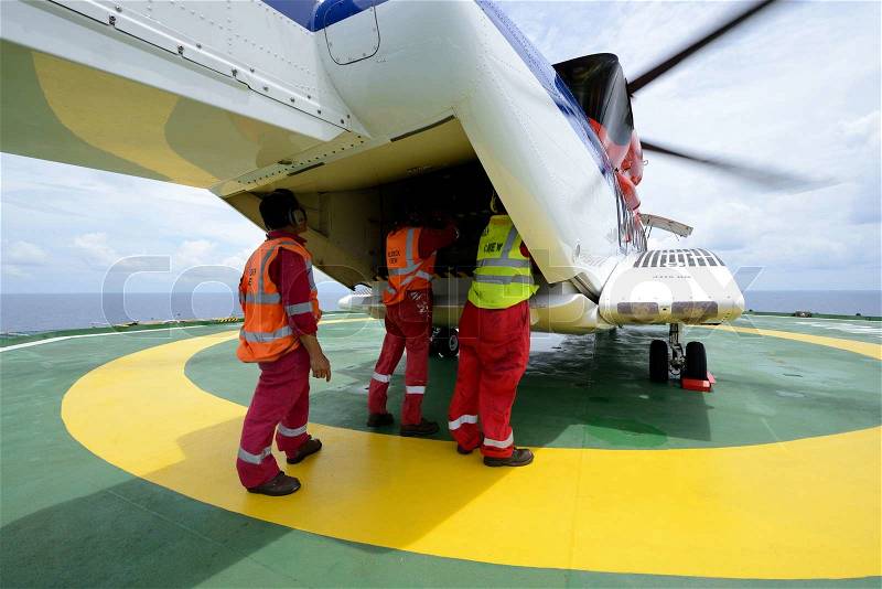 The helideck crew are loading baggage into the cargo ramp of helicopter at oil rig platform, stock photo