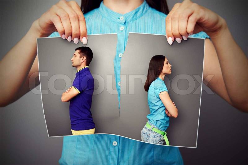 Woman lacerating photo of young couple in quarrel over dark background, stock photo
