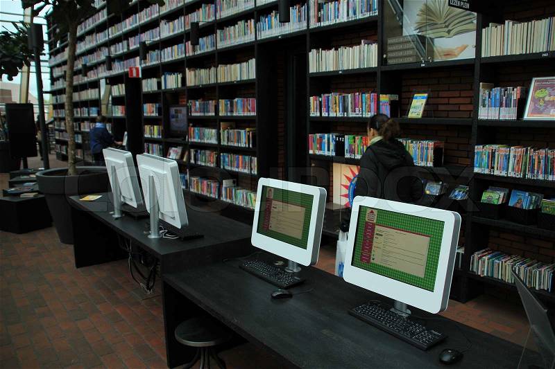 The lady is walking between all kind of books in different colours and screens in the library, stock photo
