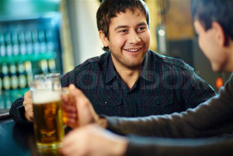 Happy man with glass of beer looking at his friend in pub, stock photo