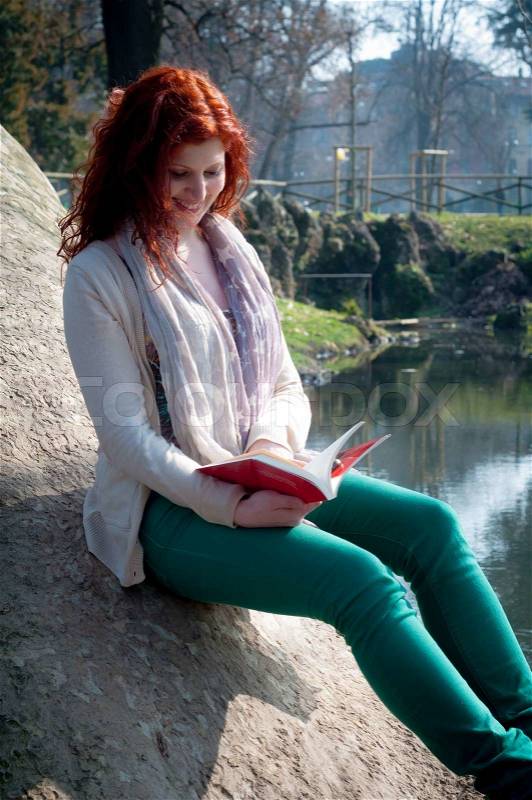 Beautiful red head young woman reading book in the park, stock photo