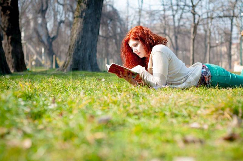 Beautiful red head young woman reading book in the park, stock photo