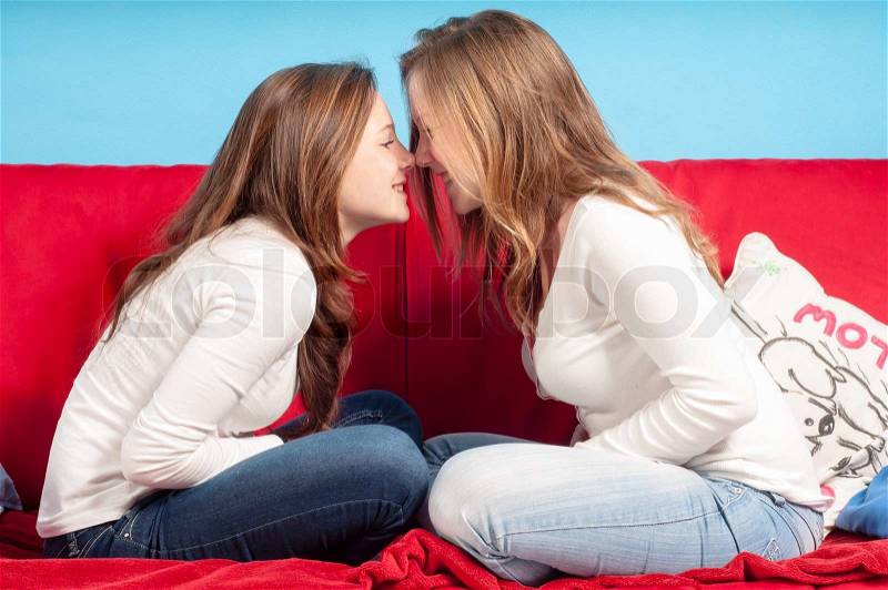 Sisters playing nose to nose on the couch in the living room, stock photo