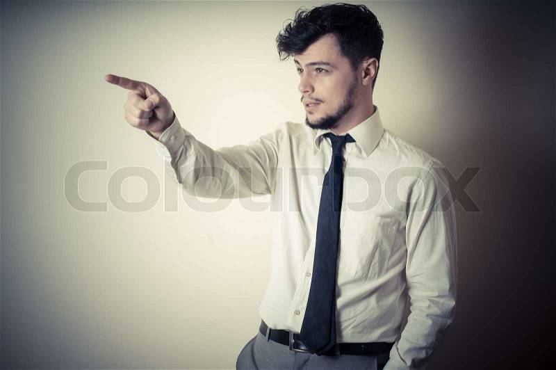 Stylish modern guy with white shirt pointing on gray background, stock photo