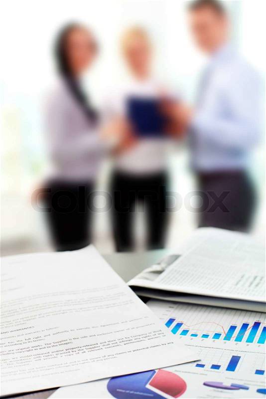 Close up of business graphs with blurred figures of office workers in the background, stock photo