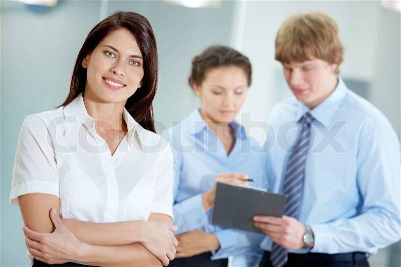 Portrait of beautiful secretary in white shirt looking at camera on the background of co-workers, stock photo