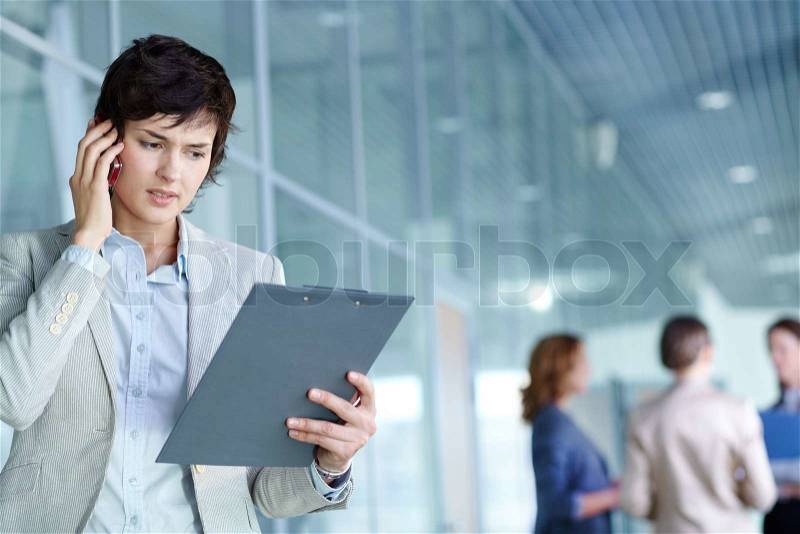 Image of busy female calling on the phone and reading document in working environment, stock photo