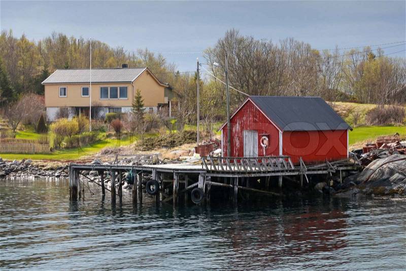 Traditional Norwegian red wooden fishing boat barn on the sea coast in spring, stock photo