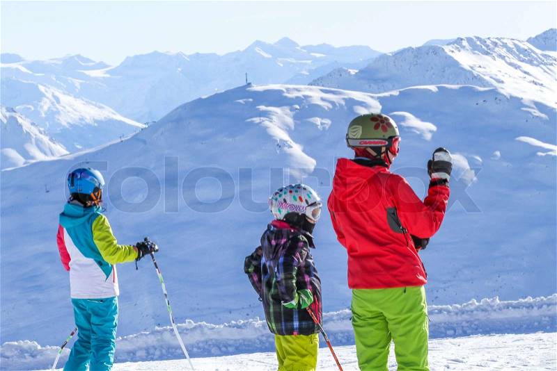 Three Skiers in Colorful Ski Clothes Looking at Sunny Mountains, stock photo