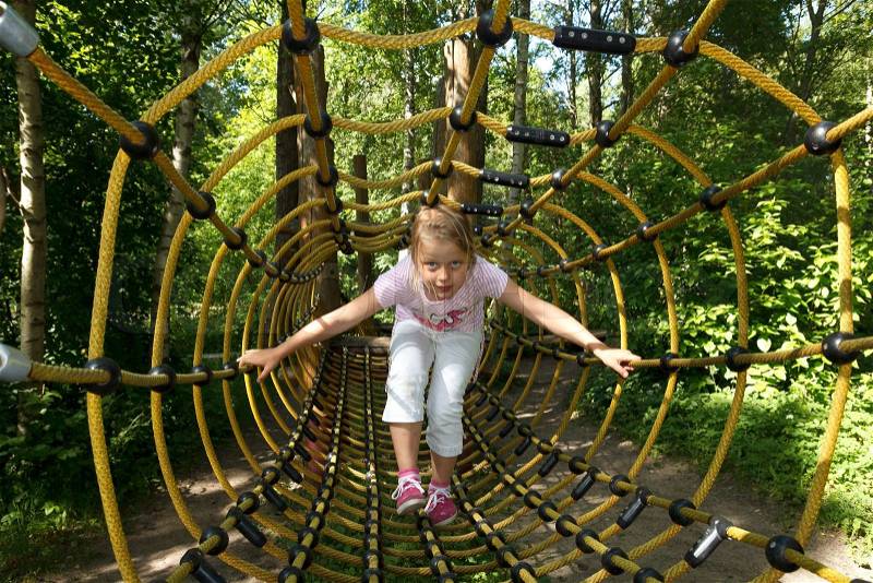 Little girl going trought tunnel in forest attraction park, stock photo