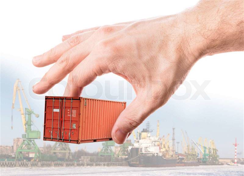 Bright red metal freight shipping container in man\'s hand above port background, stock photo