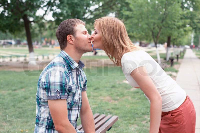 Young couple kissing on bench in park, stock photo