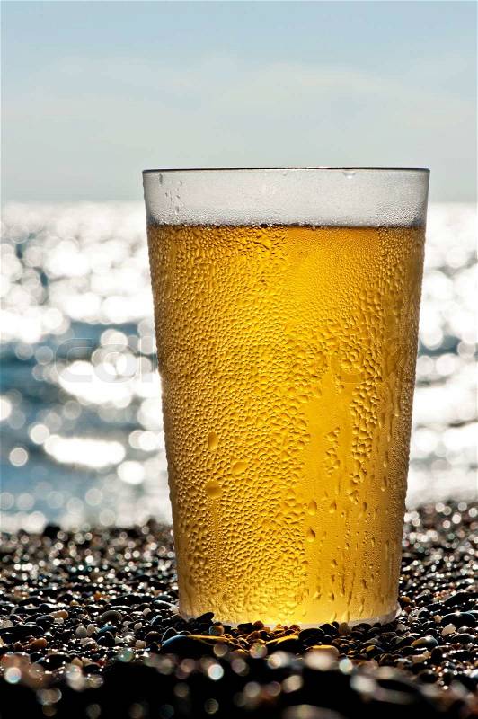 Plastic cup of beer standing on the sand by the sea, stock photo