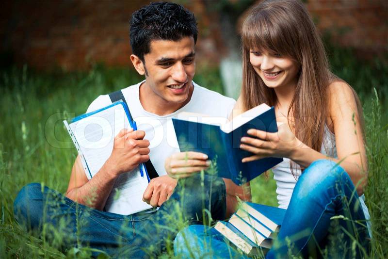 Two students guy and girl studying in park on grass with book outdoors, stock photo
