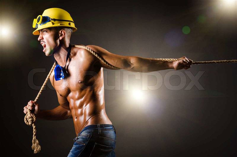 Nude builder pulling rope in darkness, stock photo