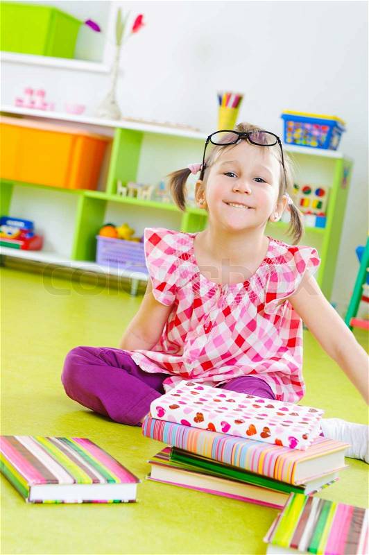 Funny little girl in glasses with books on floor, stock photo