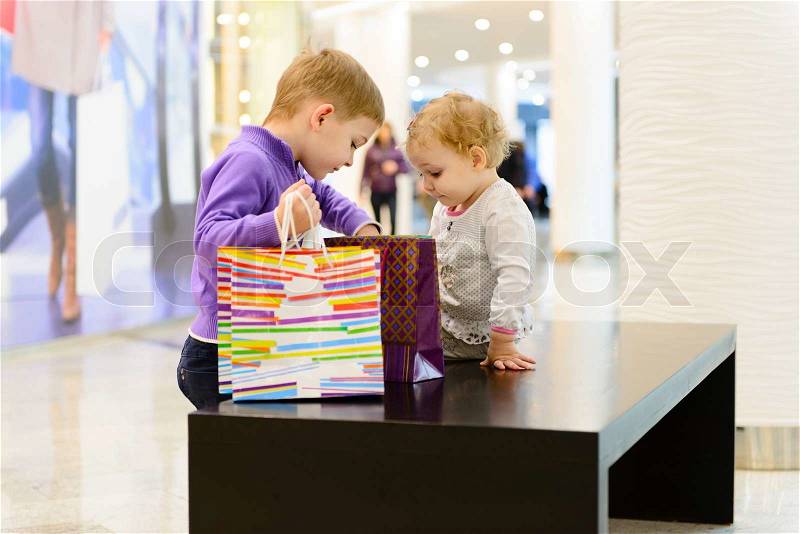 Cute little boy and girl inspecting shopping bags in mall, stock photo