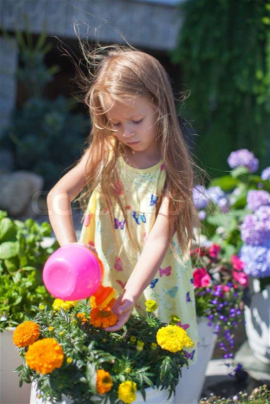 Little toddler girl watering flowers with a watering can, stock photo