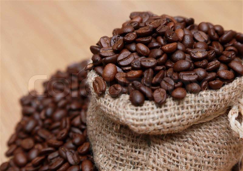 Coffee beans in a burlap bag on a wooden table, stock photo