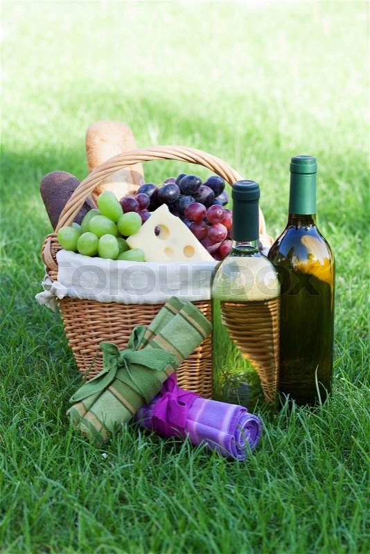 Outdoor picnic basket with bread, cheese and grape and wine bottles on lawn, stock photo