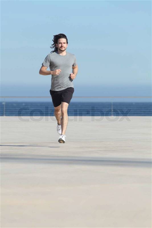 Front view of a sportsman running on the concrete of the seafront with the sea in the background, stock photo