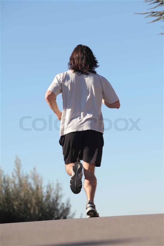 Back view of a man running on a road with the sky in the background, stock photo
