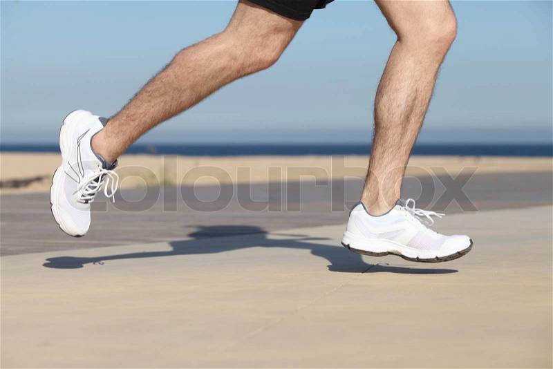 Side view of a man legs running on the concrete of a seafront with the sky in the background, stock photo