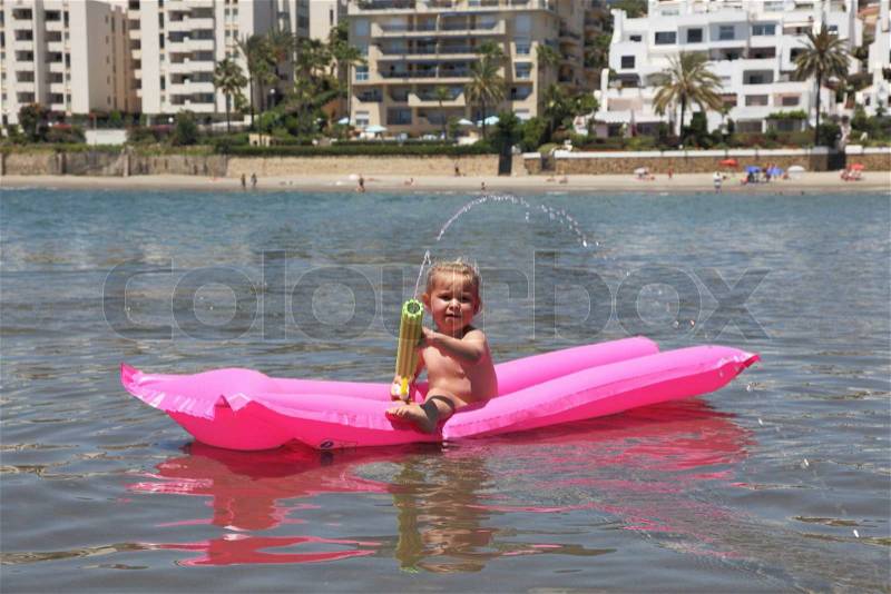 Girl swimming on an air mattress and shooting with a water pistol. Estepona, Andalusia Spain, stock photo