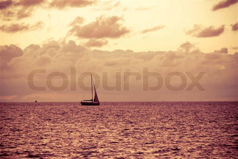 A solitary sailboat in the open sea at the sunse, vintage look, stock photo