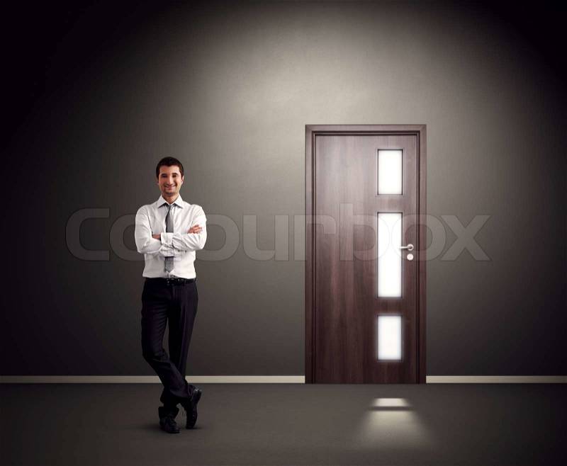 Successful businessman standing against wall with door, stock photo