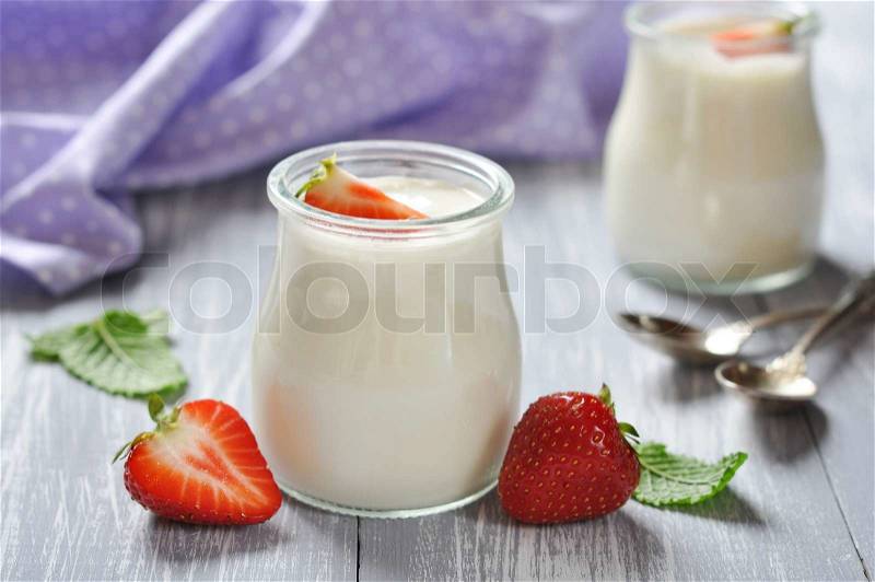 Yogurt with ripe fresh strawberry in jars on wooden background, stock photo