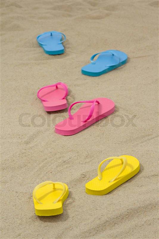 Three pairs of colorful flip flops on white sand, stock photo