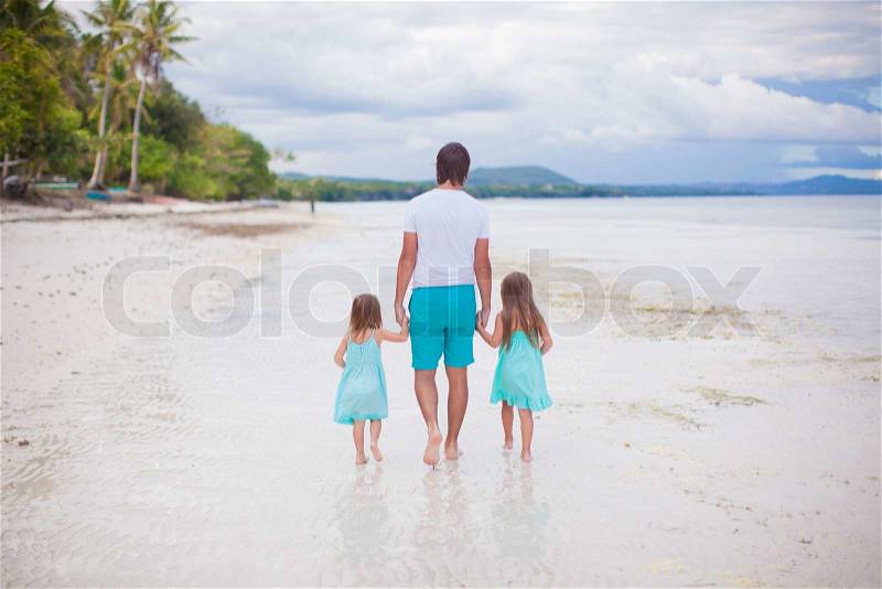 Back view of father and his two little daughters walking by the sea, stock photo