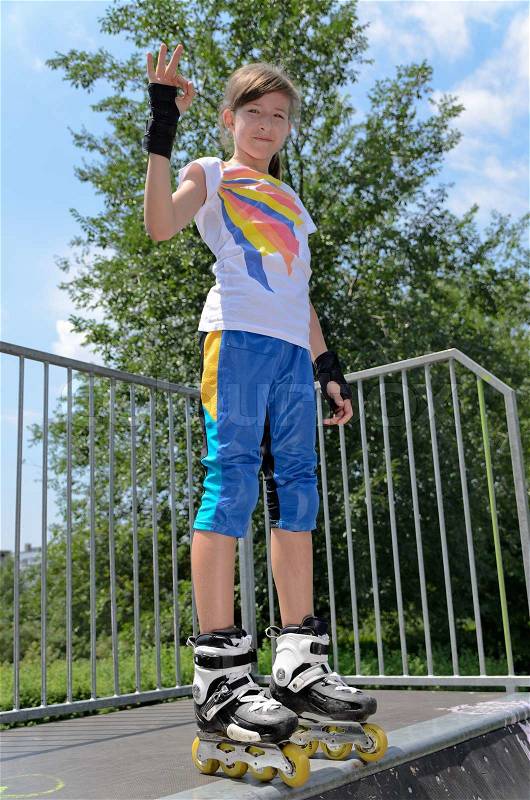 Pretty young teenage roller skater standing on top of a ramp at a skate park looking at the camera and giving a Perfect gesture with her fingers, stock photo