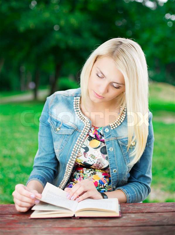 Portrait of beautiful young woman with book on green background of city park, stock photo