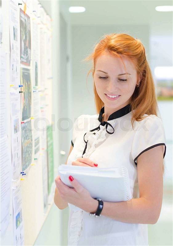Young female student looking through job offers on board, stock photo