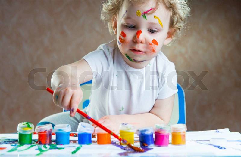 Cute little child painting with paintbrush and colorful paints, stock photo