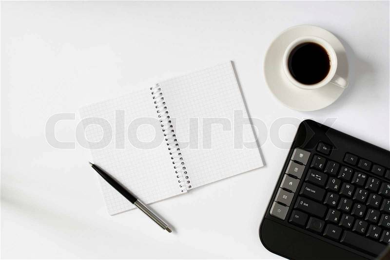 Conceptual overhead image of someone enjoying coffee in the office with a cup of espresso standing alongside an open blank notebook with a pen and a computer keyboard, stock photo