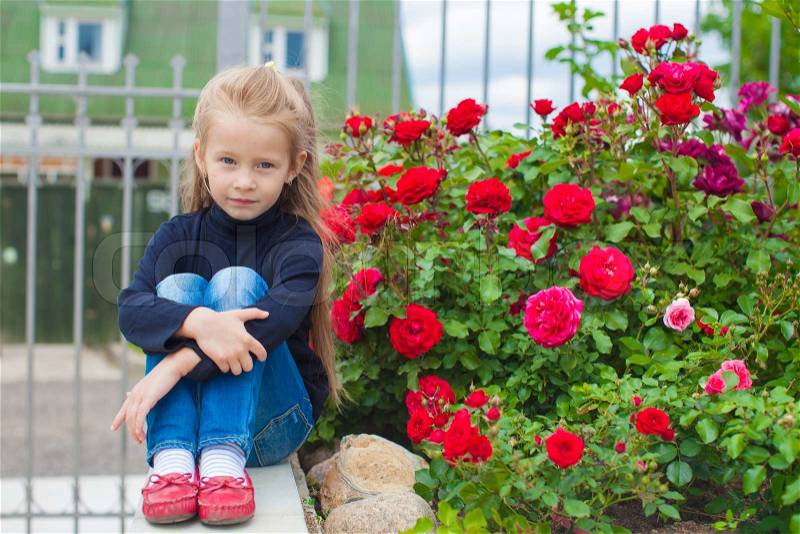 Portrait of cute little girl near the flowers in the yard of her house, stock photo