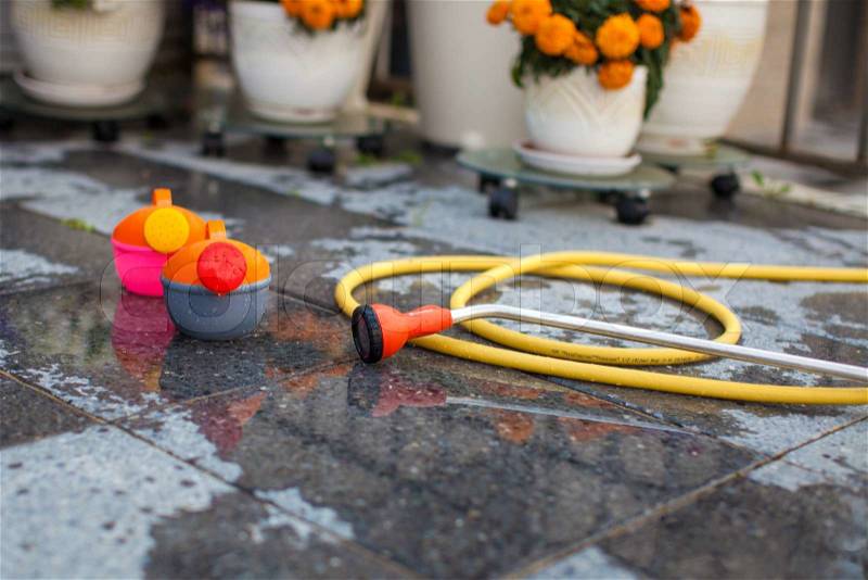 Children\'s bright watering can and a long hose on the wet ground in the yard, stock photo