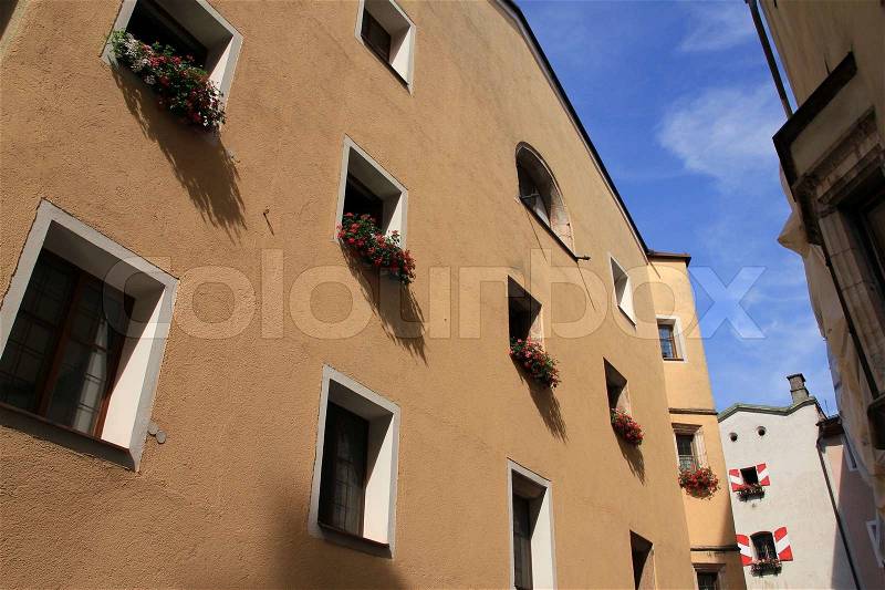 Window boxes with blooming geraniums on the painted wall of the house in summer time, stock photo