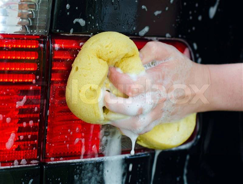 Female hand with yellow sponge washing car, stock photo