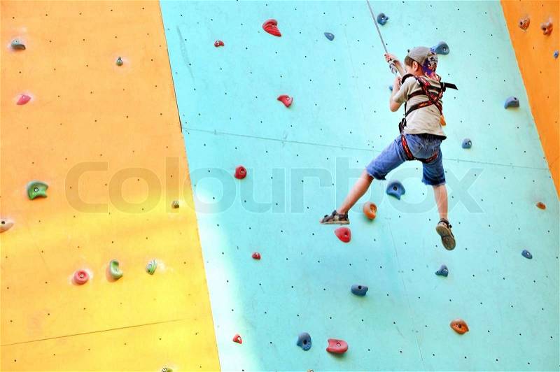 Little 6 years old boy climbing up the wall, stock photo