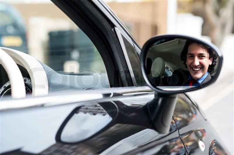 Businessman smiling in rear view mirror, stock photo