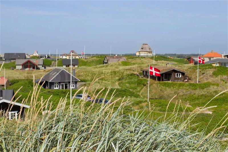 Danish holiday houses scattered among the sand dunes at the North Sea coastline in Soendervig, Denmark. Picture taken on a sunny summer day. Danish flags are visible on the picture, stock photo