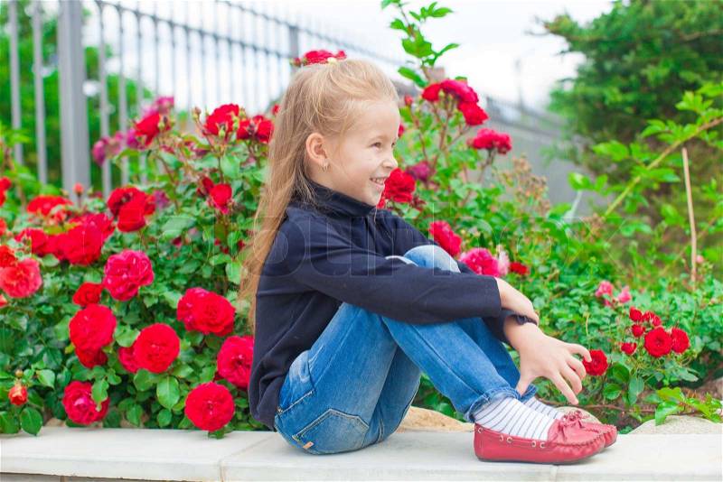 Cute little girl near the flowers in the yard of her house, stock photo